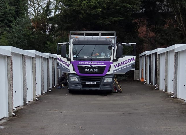 garage-istallation - Hanson Battery Garages MAN delivery truck with purple Hanson banners across its doors parked on a narrow bridge, workers nearby under the truck.